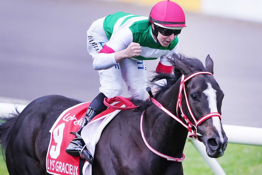 A jockey in green and white silks pumps his fist while riding a horse.