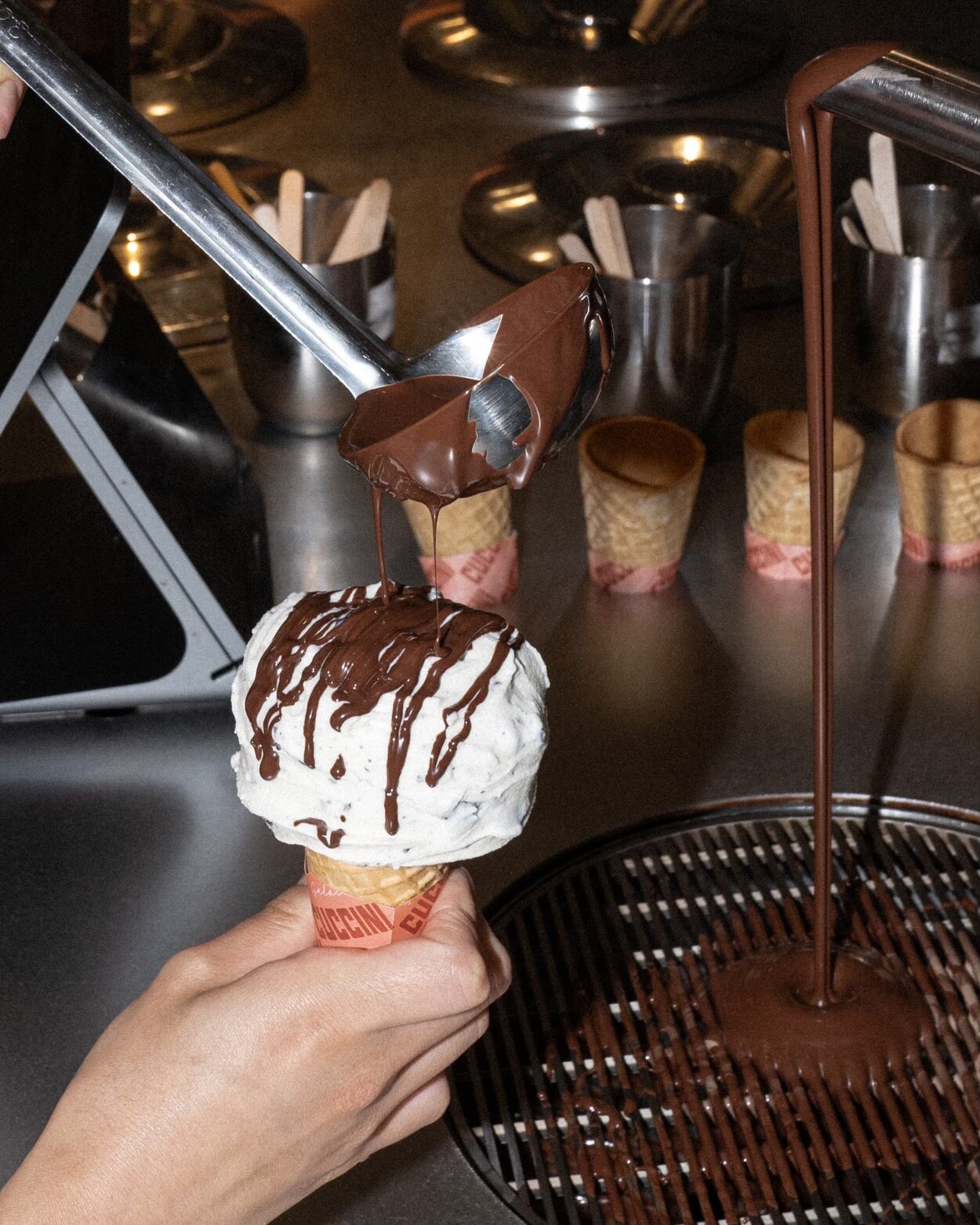 Hand holding a scoop of gelato with chocolate flowing down 
