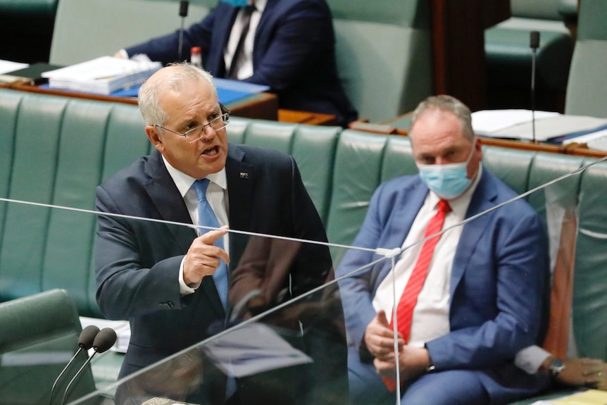 Morrison stands pointing his finger, as Barnaby Joyce wearing a masks sits behind him watching on.