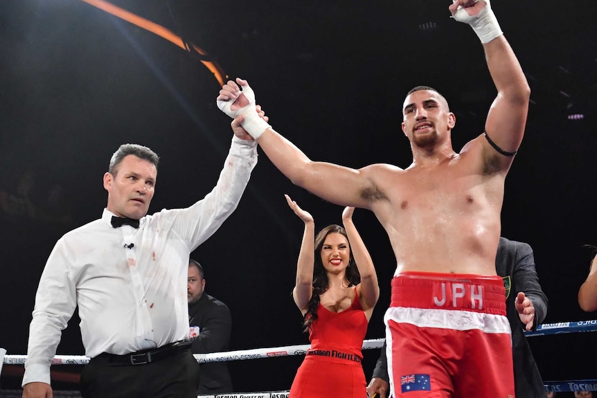 The referee holds up Justis Huni's arm the boxer celebrates his win in the ring