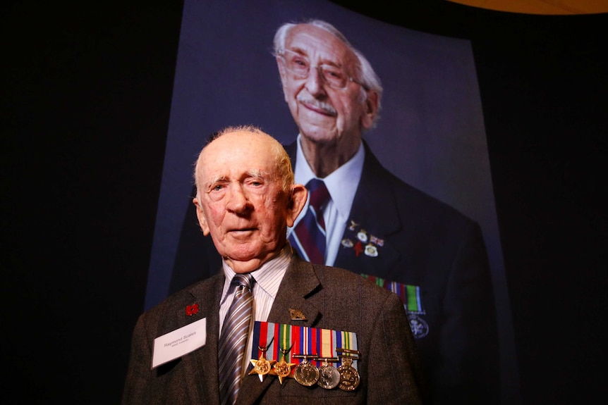 Raymond Scales stands in front of a projected portrait