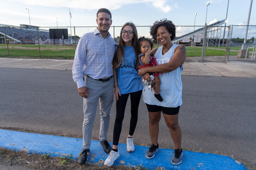 A man, a teenaged girl and a woman cradling a small child at a sports field 