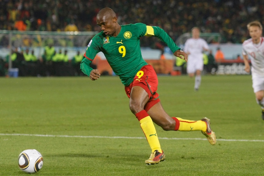 A football player in green shirt and green shorts kicks a ball.