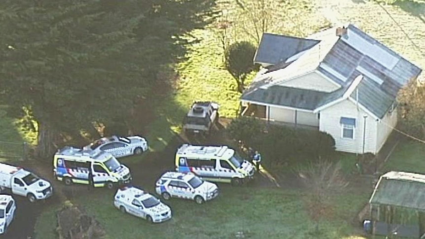 Several police cars and ambulances sit on the lawn outside a house.