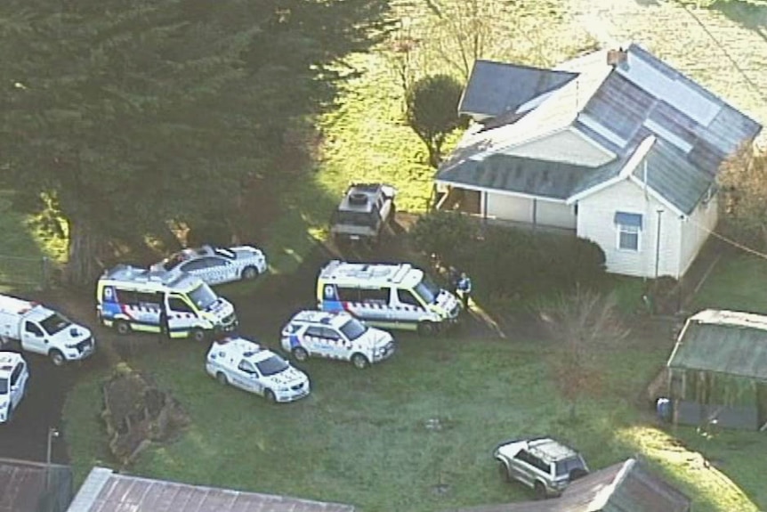 Several police cars and ambulances sit on the lawn outside a house.