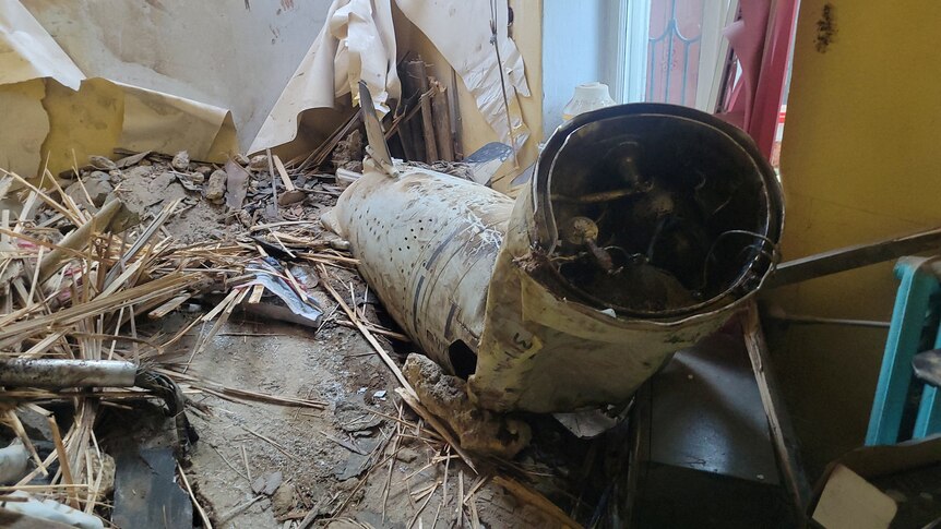 The bend, tubular shell of a missile lies in a damaged building.