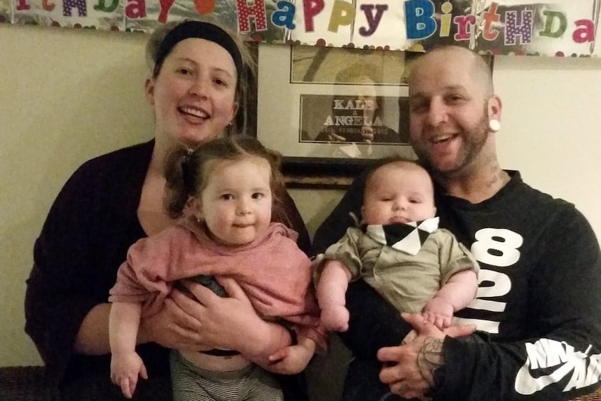 A woman and her husband pose with two young children.