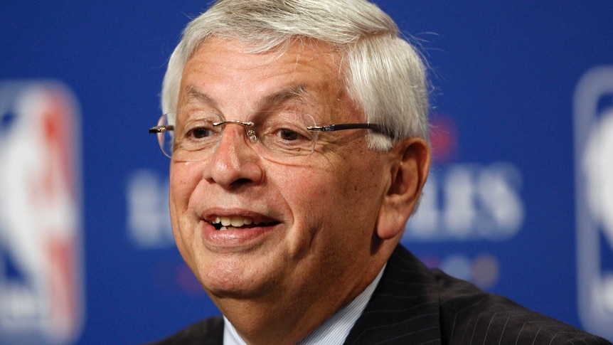 David Stern wearing a suit and glasses speaks at a microphone in front of the NBA logo
