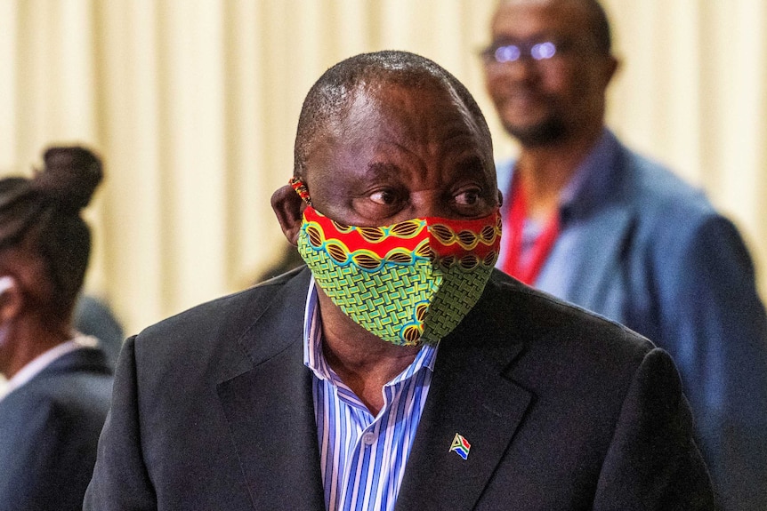 Cyril Ramaphosa is seen wearing a colourful face mask while standing among health care workers