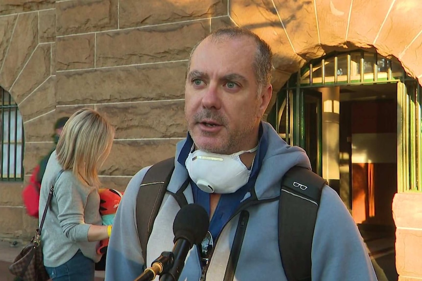 A man in grey sweater looking annoyed outside a hotel.