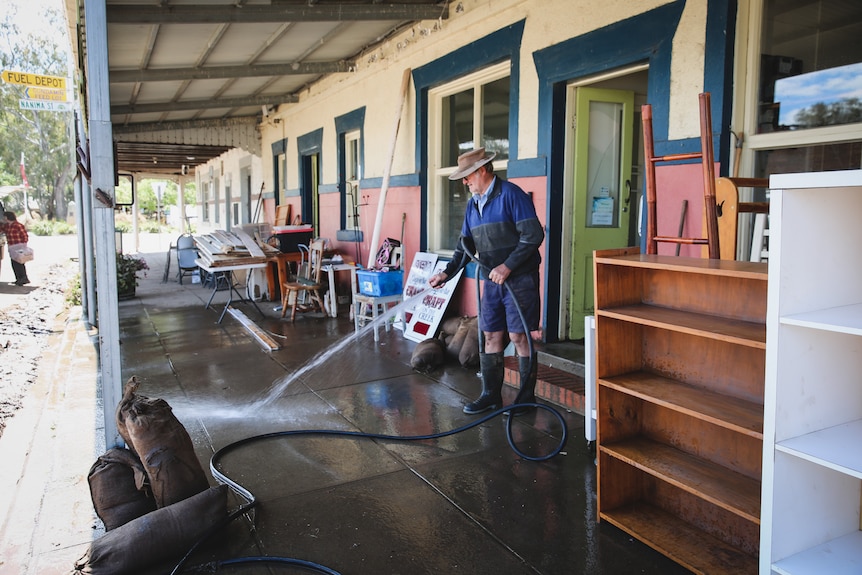 Man hoses down footpath outside a long building