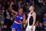 A Western Bulldogs player raises his finger in celebration of a goal, as a St Kilda player looks dejected in the background. 
