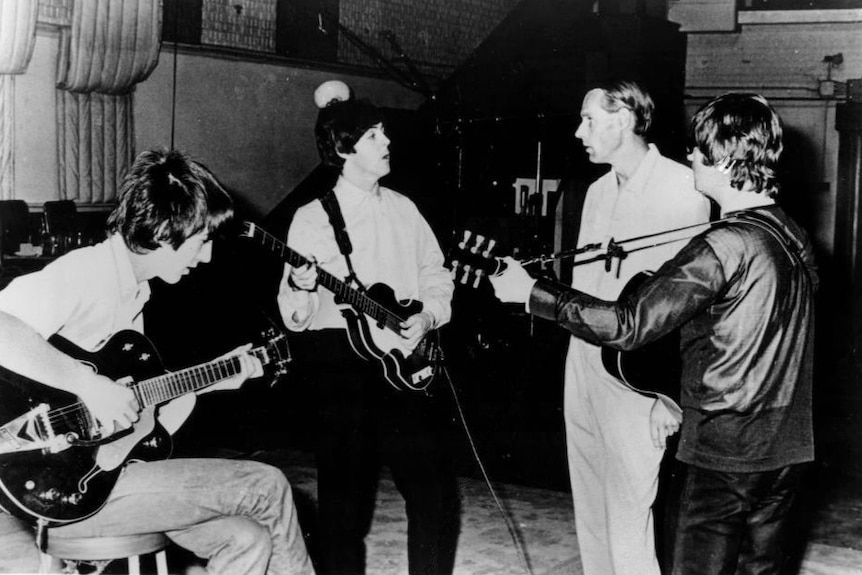 A black and white photo of George Harrison, Paul McCartney and John Lennon and producer George Martin in a studio.