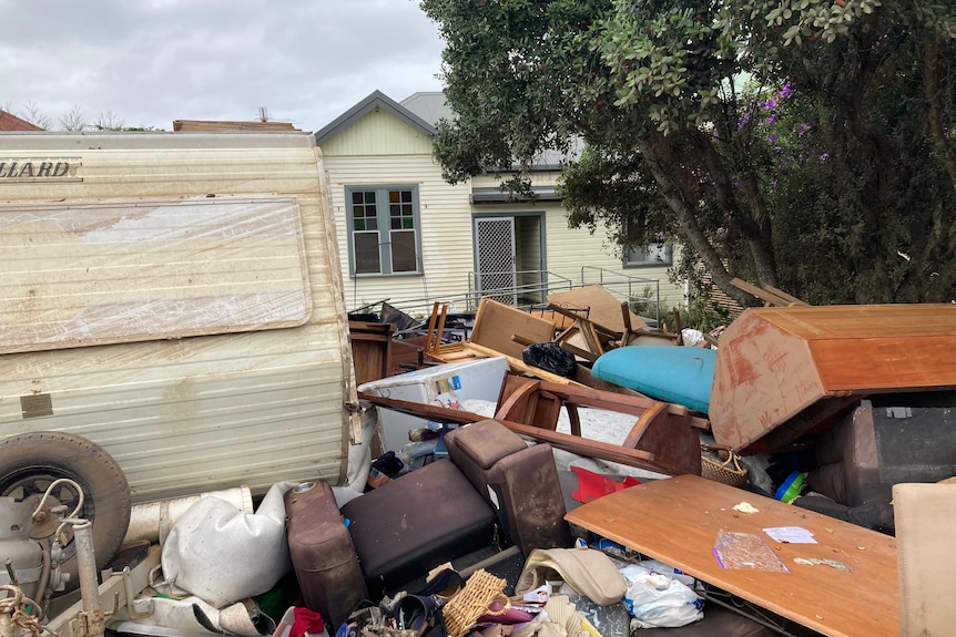A house with a ramp, and a caravan and pile of furniture and rubbish in the front yard.