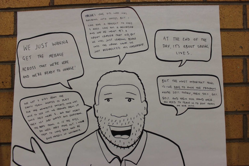 A photo of a poster featuring a man with quotes and statements in speech bubbles about the work of the Wilcannia men's group.