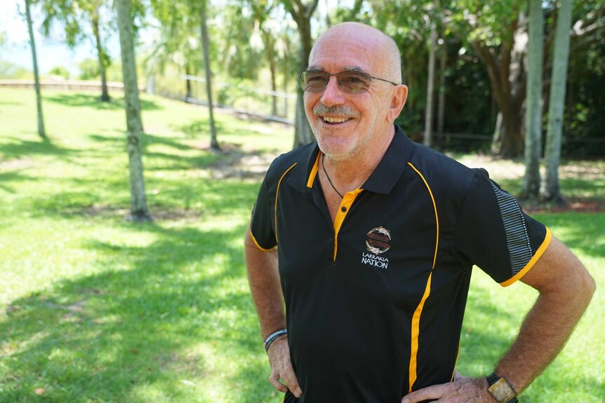 Robert Cooper is wearing a black Larrakia Nation polo and smiling at the camera. He's outside in the sun.