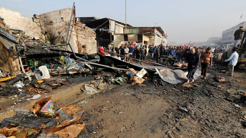 A marketplace is destroyed where a car bomb exploded, people crowd around to look at the damage