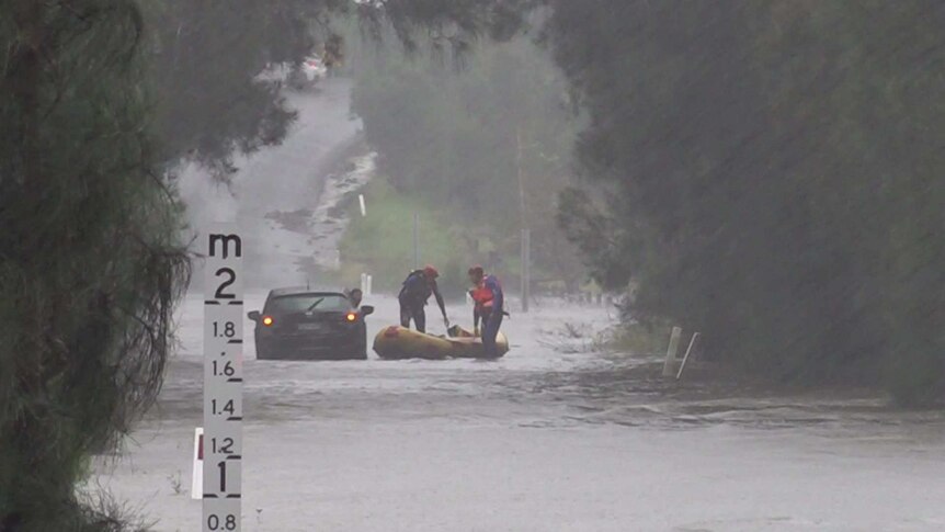 Two men manoeuvre a yellow inflatable dinghy near a car in floodwaters.