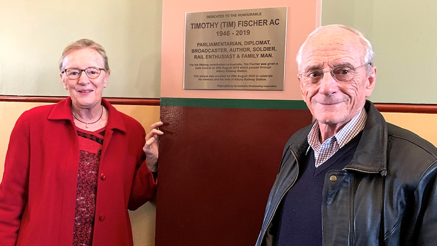Vicki Baudry and Dr Tony Fischer standing in front of a memorial plaque for Tim Fischer at the Albury Train Station