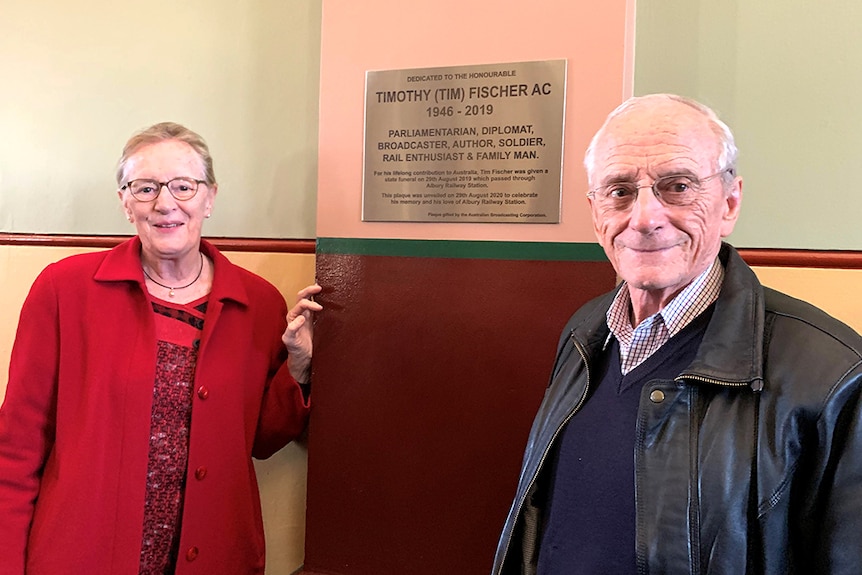 Vicki Baudry and Dr Tony Fischer standing in front of a memorial plaque for Tim Fischer at the Albury Train Station