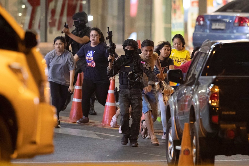 Thai security force members with large guns escort a group of people to safety outside a shopping centre.