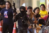 Thai security force members with large guns escort a group of people to safety outside a shopping centre.