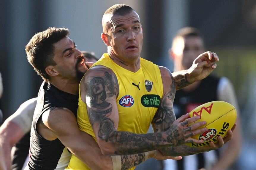 Richmond AFL player Dustin Martin holds onto the ball as he is grabbed around the waist by a Collingwood defender.