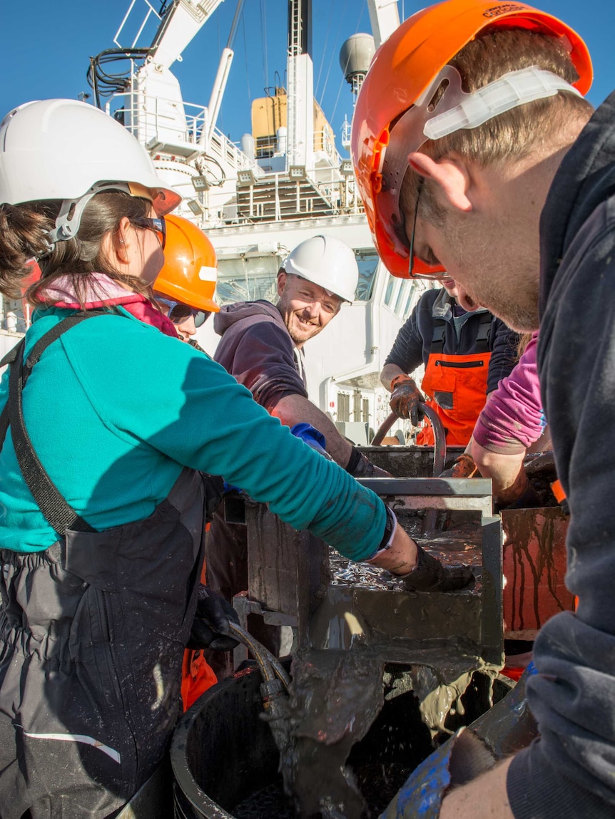 Crew with hard hats working on deck of ship.