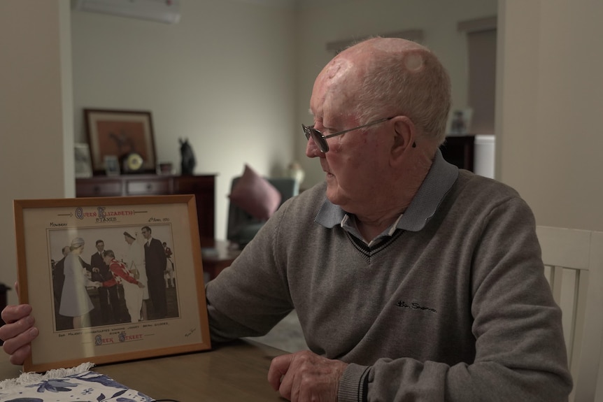 An elderly man holds and looks at a framed photo