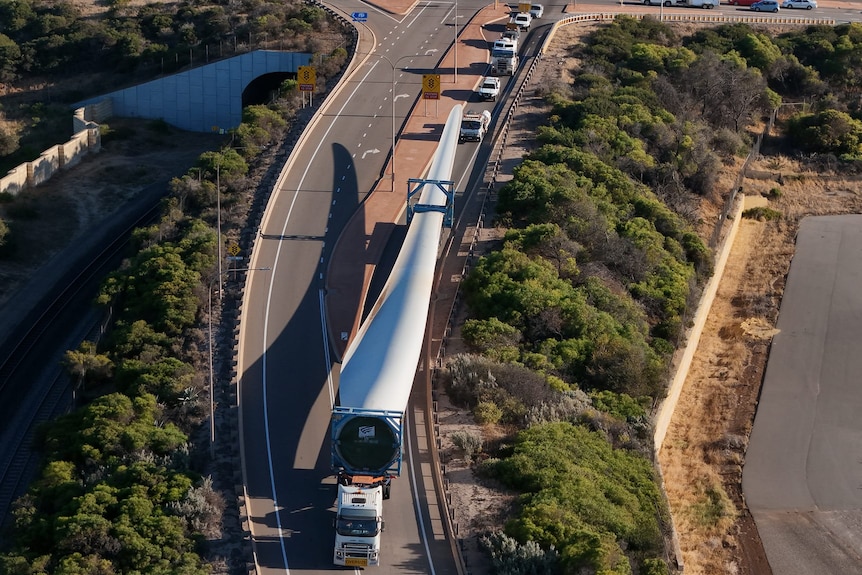 An aerial view of a truck carrying a wind turbine blade under escort.  