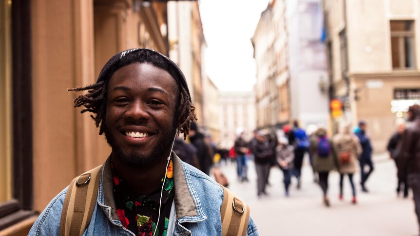 A man walks down the street listening to earbuds and smiling.