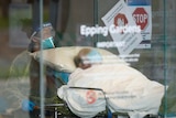 A man wearing a face mask in a hospital bed is wheeled out by a health worker in a face shield and mask.