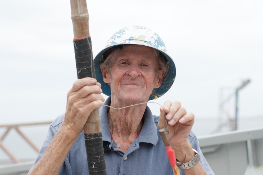 Close up of old man's face smiling at camera holding a bamboo fishing pole and lure