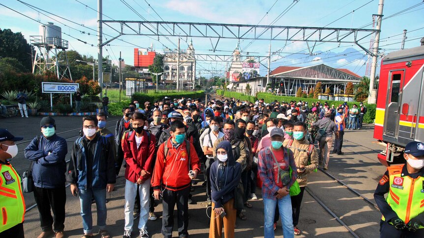 Tens of men and women in Indonesia stand on train tracks with masks on near two policeman.