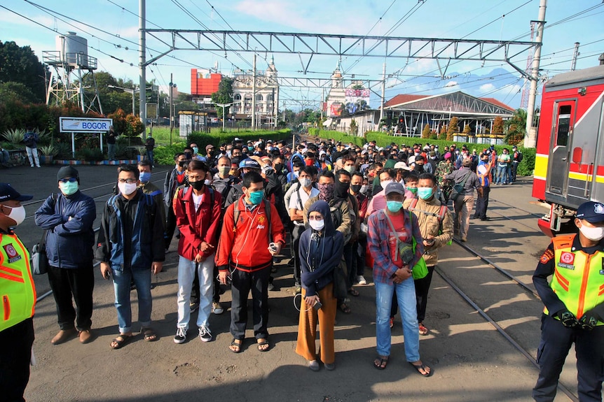 Tens of men and women in Indonesia stand on train tracks with masks on near two policeman.