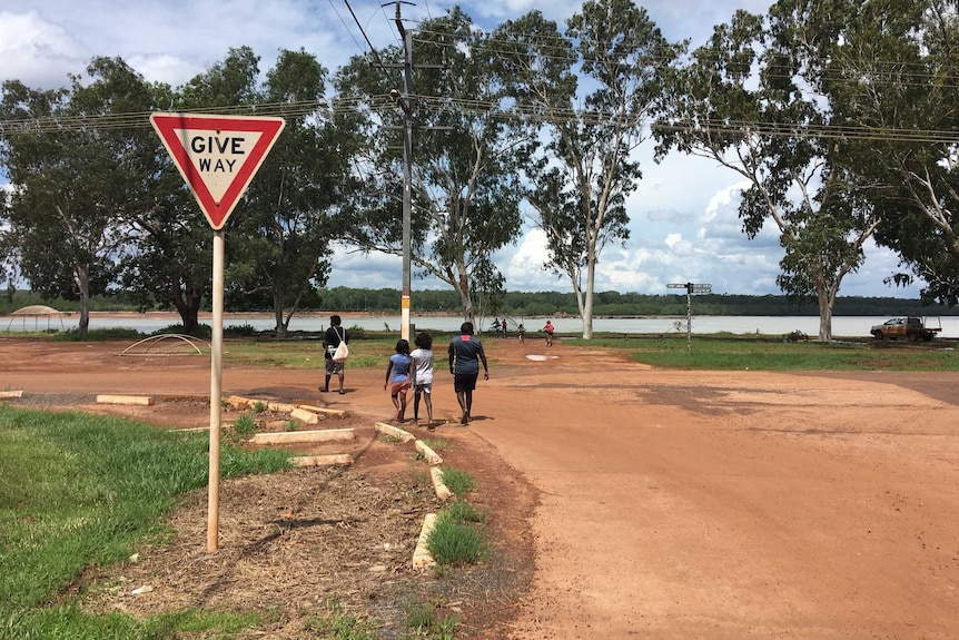 A few people walk down a dirt road with water in the distance.