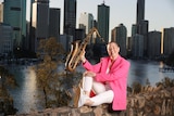 Shelley Bishop holding up a saxophone with the Brisbane River and city in the background