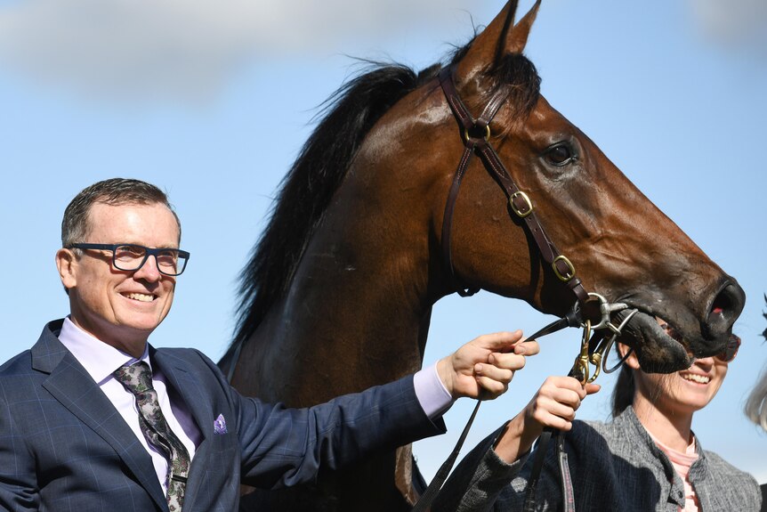 a man in a suit and glasses smiling and posing with a horse outdoors