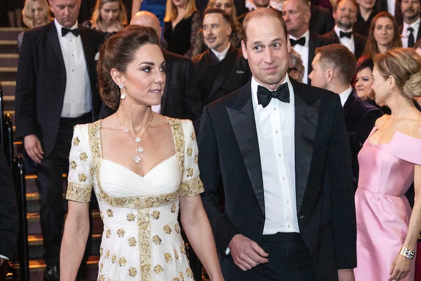 Kate Middleton wears a white gown with gold embellishments. Prince William is in a black tuxedo.