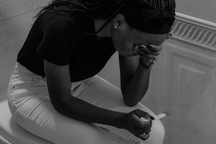 A black and white photo of a woman looking upset at a pregnancy test in her hand