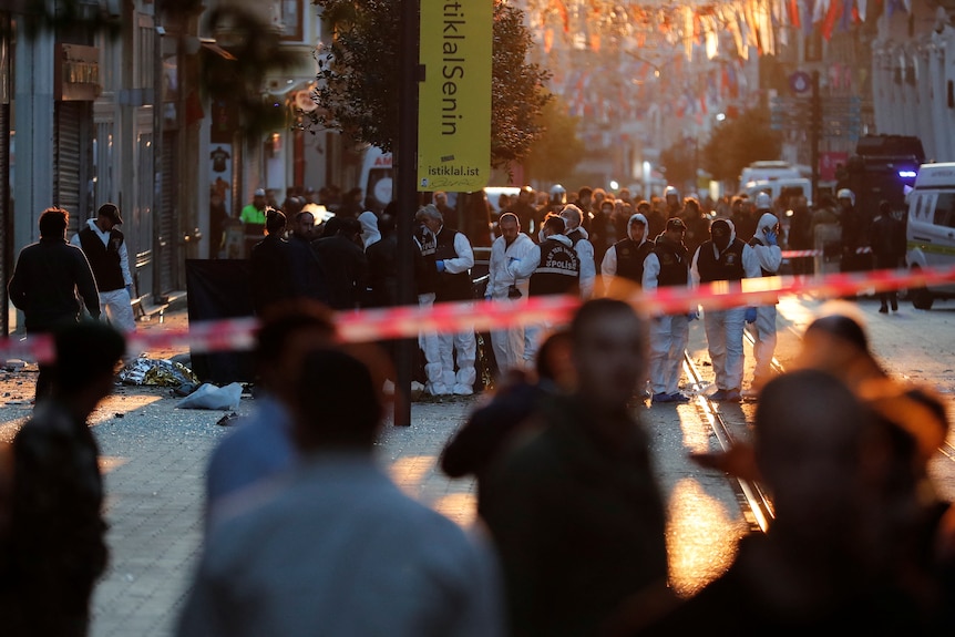 Police and emergency services work behind a cordon at the scene of an explosion on a busy pedestrian street.