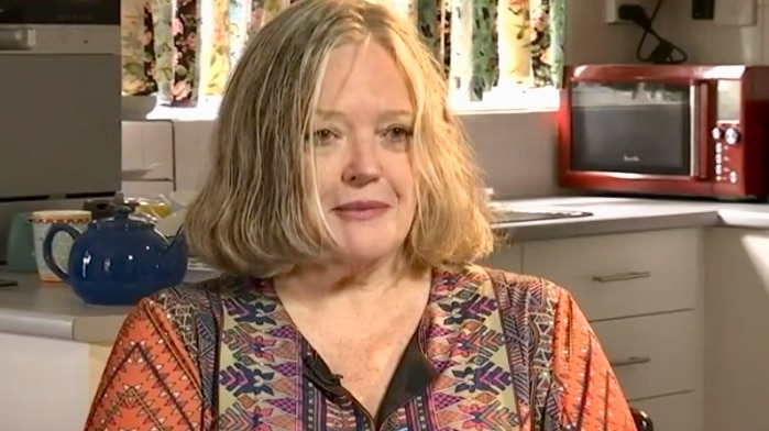 A woman with shoulder-length blond hair sitting at a kitchen table.