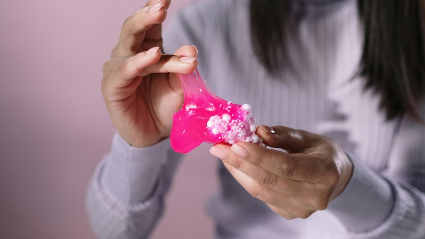 A close-up of a woman hands playing with pink and white slime.