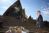 Bill Shorten stands with his hands in his pockets in front of some flowers on the steps of the Sydney Opera House.