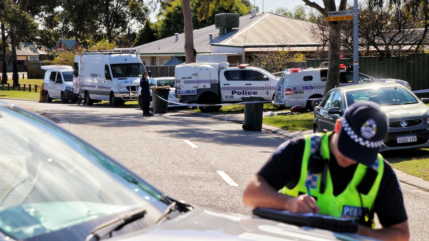 An officer writes notes in a folder outside a house in Ballajura, which is cordoned off with police tape.