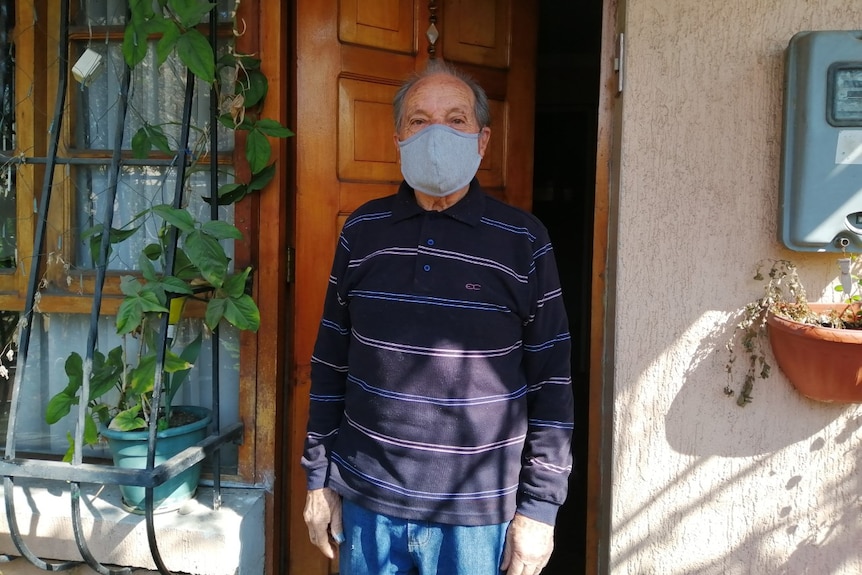 An older man standing in a doorway wearing a face mask.