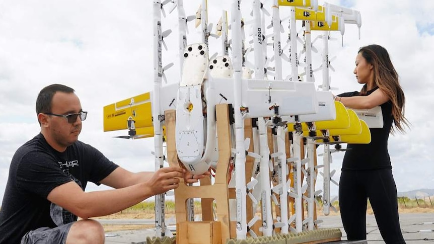 Two people help arrange drones on a trolley