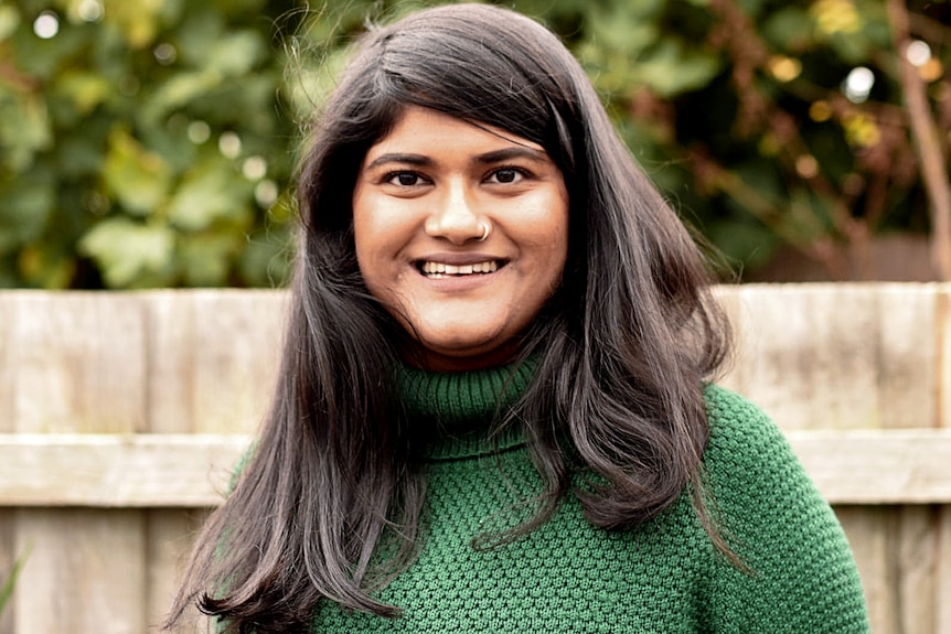 A woman in a green jumper smiling, for a story on choosing to get the AstraZeneca vaccine at 35.