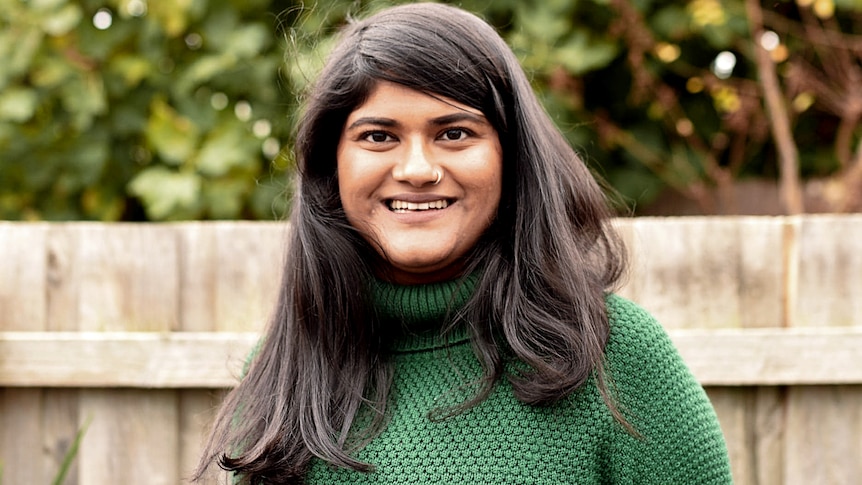 A woman in a green jumper smiling, for a story on choosing to get the AstraZeneca vaccine at 35.