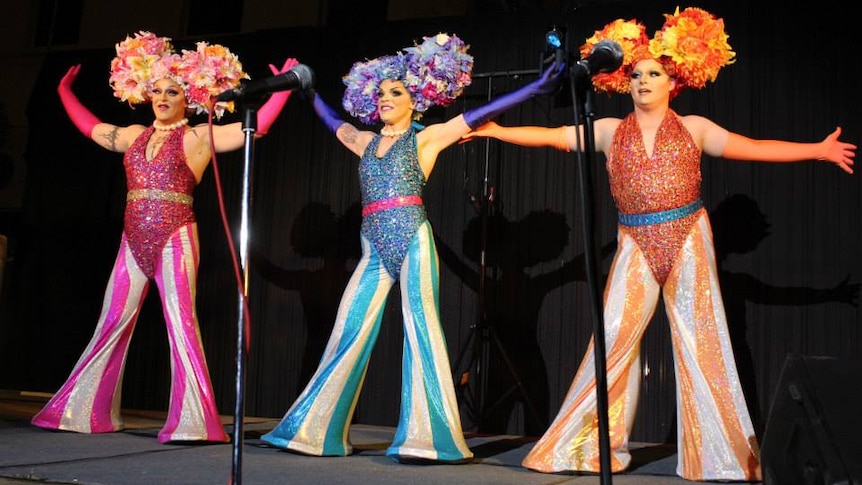 Three drag queens dancing on stage.